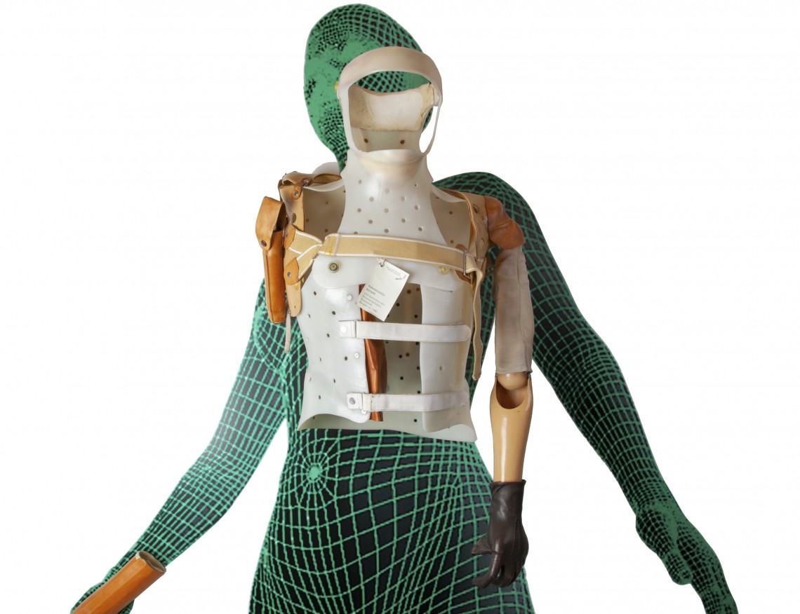 Zwei wandmontierte Oberkörper-Korsette vor einer Abbildung einer als CAD-Wireframe digital modellierten menschlichen Person