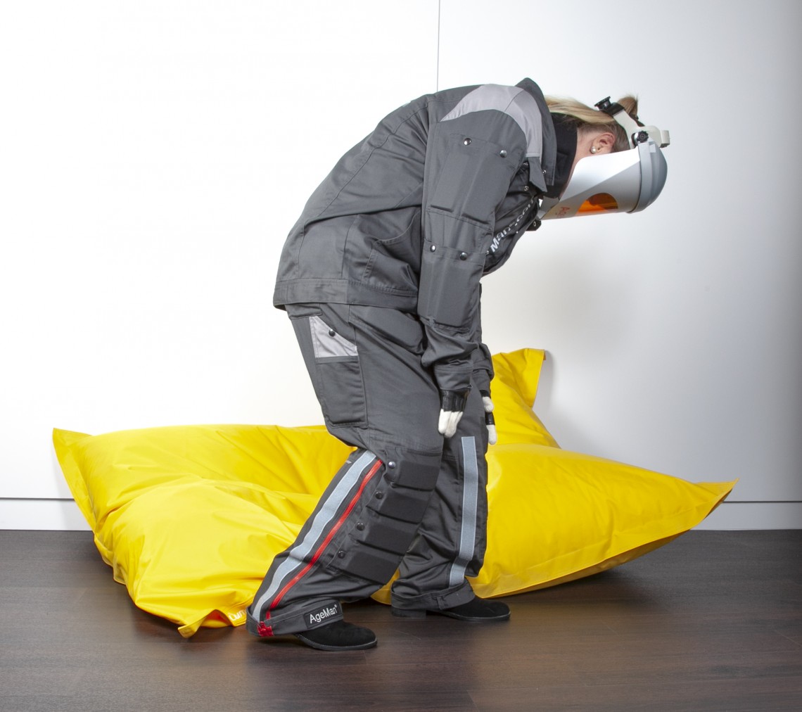 Junge Frau mit angelegtem AgeMan Alterssimulationsanzug beim Aufstehen von einem Fatboy Sitzkissen - Phase 3