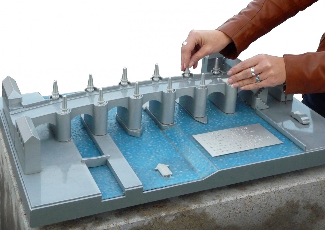 Nahaufnahme von weiblichen Händen beim Ertasten des Blinden-Tastmodells der Alten Mainbrücke in Würzburg