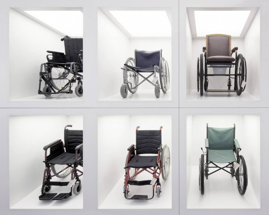 In Leuchtboxen wie Designer-Stücke präsentierte sechs verschiedene Rollstühle aus dem Sammlungsbereich der Ausstellung